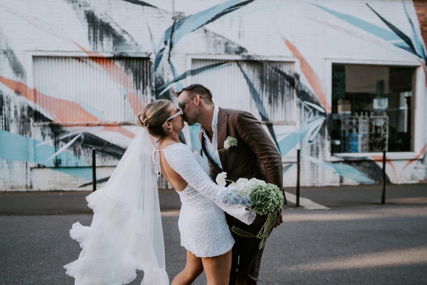 Newlyweds kissing in front of a painted mural wall in Toowoomba